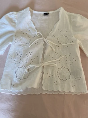 Vit broderad blus med knytband - Söt vit blus från Gina Tricot med broderade blommor och hålmönster framtill. Blusen har knytband framtill, vågig kant och puffiga korta ärmar. Den är i storlek xs💓