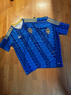 Blå Sverige fotbollströja Adidas - Säljer en blå Sverige fotbollströja från Adidas med retroinspirerat mönster, gula detaljer och tre ränder på axlarna. Perfekt för nu till VM nu i sommar, 1 av tröjorna 249, båda för 450kr! Båda i storlek M. Köpte för nån månad sedan men gillar de ej, så jar använt 1 av tröjorna 2-3 gånger! 