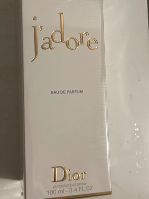 J'adore Eau de Parfum 100ml från Dior - J'adore Eau de Parfum från Dior i en elegant vit kartong med guldiga detaljer. Flaskan innehåller 100 ml och är en klassisk doft från Dior, perfekt för dig som gillar lyxiga och feminina parfymer. Förpackningen är stilren och exklusiv.