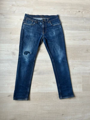 Blåa Dry Nudie Tape Ted Jeans Storlek W36 L32 - Mycket fina Nudie Jeans i blå färg. Jeansen är i mycket bra skick och sparsamt använda. |  Äkta som allt annat jag säljer! ✅ |  Storlek: W36 L32 | Skick: Mycket Bra Skick - ett hål som har blivit lagat (SE SISTA BILD) | Färg: Blå | Märke: Nudie | Modell: Jeans |   Hör gärna av dig vid frågor så svarar jag så fort jag kan! 😁 | (SKU - 118) 