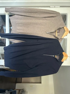 Två halvzip-tröjor i ullmix - Två stilrena halvzip-tröjor från Oscar Jacobson, en i mörkblått och en i beige. Båda har hög krage med dragkedja och är tillverkade i mjuk ullmix. Perfekta för lager-på-lager och snygga till jeans eller chinos.