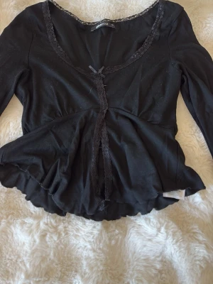 Svart blus med spets och rosett - Svart blus från Gina tricot  med lång ärm, spetsdetaljer längs halsringningen. Söt liten rosett vid halsen och lätt peplumformad nederkant. Perfekt för dig som gillar romantiska detaljer och enkel stil. Skriv för frågor❤️
