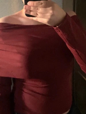 Vinröd offshoulder topp - Trendig vinröd offshoulder topp med långa ärmar och tight passform. Toppen har en croppad längd och är tillverkad i ett stretchigt material som sitter snyggt mot kroppen. Perfekt för dig som vill ha en stilren men ändå iögonfallande look.