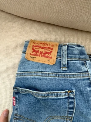 Levi's 502 Regular Taper jeans blå - Säljer ett par klassiska blå Levi's 502 Regular Taper jeans med normal passform och avsmalnande ben. Jeansen har fem fickor, synliga sömmar och ikonisk läderpatch bak i midjan. Perfekta för en avslappnad och stilren look.