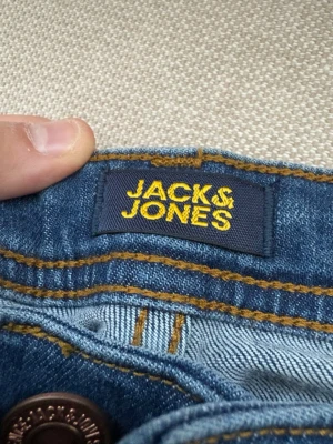 Blå jeans från Jack & Jones Regular Taper - Snygga blå jeans från Jack & Jones med klassiska gula sömmar och knappstängning. Jeansen har en tidlös passform och är tillverkade i slitstarkt denimtyg. Perfekta för dig som gillar en enkel och stilren look.