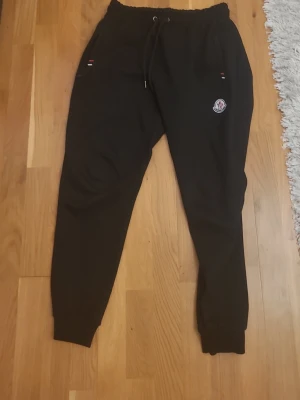 Svarta mjukisbyxor - Svarta mjukisbyxor från Moncler med dragsko i midjan och resår vid bensluten. Byxorna har två fickor framtill och Moncler-logga på vänster ben. Perfekta för en avslappnad och trendig stil.