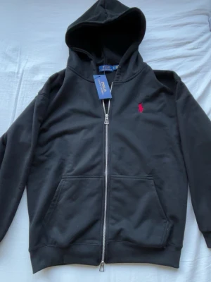Helt ny Svart  Polo hoodie - Helt ny Svart  Polo hoodie i storlek S passar även M. Inga täcken på användning så jag aldrig har använt den. Pris kan dirkuteras vid snabb affär.