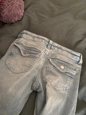 Ljusblå jeans från H&M Divided - Säljer ett par ljusblå jeans från H&M Divided i storlek 36. Jeansen har klassisk femficksdesign, raka ben och silverfärgade knappar. Materialet är mjukt denim i bomull och de har en snygg tvättad look. Perfekta till en avslappnad stil!