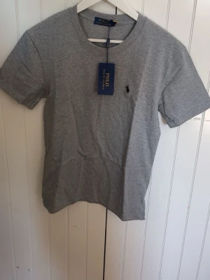 Grå t-shirt från Polo Ralph Lauren - Klassisk grå t-shirt från Polo Ralph Lauren med rund halsringning och broderad logga på bröstet. Tillverkad i mjuk bomull och har en normal passform. Perfekt basplagg med stilren design.