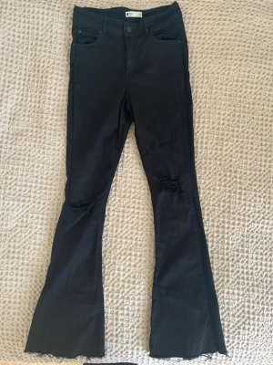 Svarta utsvängda jeans med fransning - Snygga svarta jeans från Gina Tricot med utsvängda ben, fransade knän och råa, fransiga benslut. Jeansen har klassisk femficksmodell och hög midja. Perfekta för dig som gillar en edgy stil.