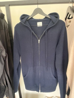 John Henric Marinblå cashmere hoodie - Mörkblå hoodie i 100% cashmere från John Henric. Tröjan har dragkedja framtill, två fickor och huva. Ny pris är 2 999 kr. Hör av er vid minsta frågan ! 