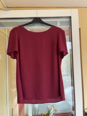Vinröd blus från Oasis, storlek 12 - .Topp med korta ärmar och en rundad halsringning. Knäpps med knapp bak.
