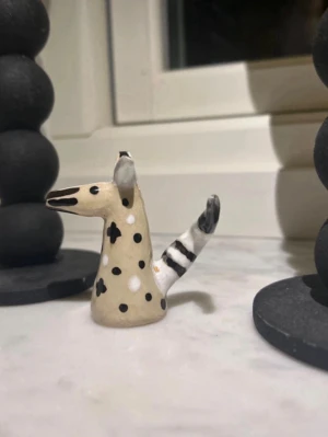 Keramisk djurfigur med prickar - Unik handgjord keramisk figur föreställande ett djurhuvud med lång nos, stora öron och randig svans. Figuren är beige med svarta och vita prickar samt svarta ränder på svansen. Perfekt som dekoration eller samlarobjekt.