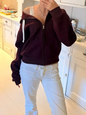 Vinröd hoodie Gina Tricot  - Säljer en populär vinröd hoodie med dragkedja och vita snören i huvan. Hoodien har två fickor framtill och är i mjukt material, perfekt för en avslappnad stil. Passar dig som gillar en enkel men snygg look. Storlek M men passar mig som S/XS! 💕Änvänd 1-2 gånger 💕