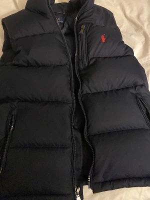 Väst från Polo Ralph Lauren inköpspris 1300 kr  - Snygg mörkblå dunväst från Polo Ralph . Västen har hög krage, två dragkedjefickor och quiltad design.