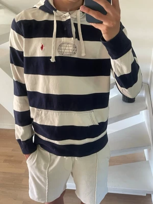 Randig hoodie från Ralph Lauren - Snygg hoodie med breda marinblå och vita ränder från Ralph Lauren. Klassisk huva med dragsko och känguruficka framtill.