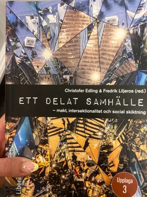 Ett delat samhälle kursbok - Kurslitteratur med titeln 'Ett delat samhälle – makt, intersektionalitet och social skiktning' av Christofer Edling & Fredrik Liljeros. Färgstarkt omslag med speglade trappmotiv och tydlig text. Upplaga 3. Perfekt för dig som pluggar samhällsvetenskap.