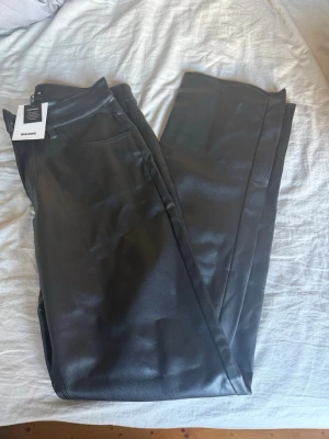 Svarta PU-byxor från Bik Bok - Snygga svarta manchesterbyxor i PU-material från Bik Bok. Modellen är low waist med raka ben och klassiska fickor. Perfekta för dig som vill ha en trendig och edgy look. Storlek 38.