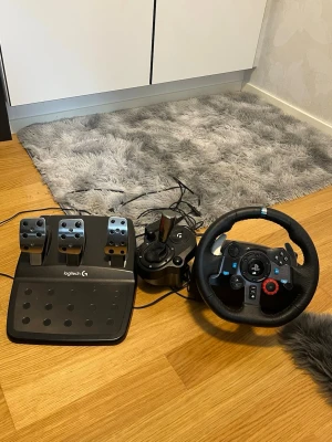 Logitech G29 ratt och pedaler med växelspak - Säljer ett Logitech G29 racing rattset med pedaler och växelspak. Ratten är svart med blå och röda detaljer, har PlayStation-knappar och är klädd i läder. Pedalerna är i metall och plast, perfekt för racing på konsol eller PC.