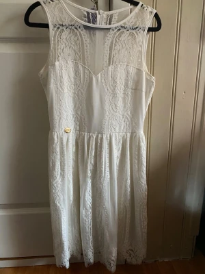 Vit studentklänning  - Superfin vit klänning med spetsdetaljer och transparent mesh upptill. Klänningen är ärmlös, har rund halsringning och markerad midja med lätt utställd kjol. Perfekt till studenten eller sommaren🌸