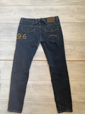 Mörkblå jeans från G-Star RAW - Snygga mörkblå jeans från G-Star RAW med raka ben och klassisk femficksdesign. Bakfickorna har dekorativa detaljer och broderad logga samt siffran 96. Jeansen är tillverkade i denim och har en låg midja. Bra skick och ser inte så använda ut. Storlek 28.