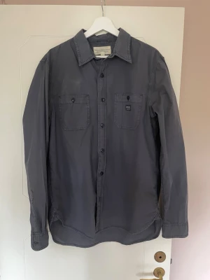 Mörkgrå skjorta Denim & Supply Ralph Lauren - Mörkgrå skjorta från Denim & Supply Ralph Lauren i storlek L. Skjortan har två bröstfickor med knappar, klassisk krage och knäppning framtill. Tillverkad i mjukt bomullstyg, perfekt för en avslappnad men snygg look. 