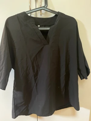 Svart blus med v-ringning - En stilren svart blus med v-ringad hals och trekvartsärmar. Blusen har en rak passform och är tillverkad i ett lätt tyg/polyester som ger en avslappnad look. Perfekt att matcha med jeans eller kjol för en trendig outfit. L men mer som en Medium 