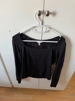 Svart långärmad topp från H&M - En svart långärmad topp från H&M med bred, fyrkantig urringning. Enkel och stilren design som passar till många olika outfits. Tillverkad i mjukt material som känns skönt mot huden.