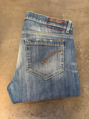 Ljusblå jeans från Dondup W34 - Snygga ljusblå jeans från Dondup med klassisk femficksdesign och diskreta slitningar framtill. Jeansen har raka ben och kontrastsömmar, samt en unik broderad detalj på bakfickan. Perfekta för en trendig och avslappnad stil.