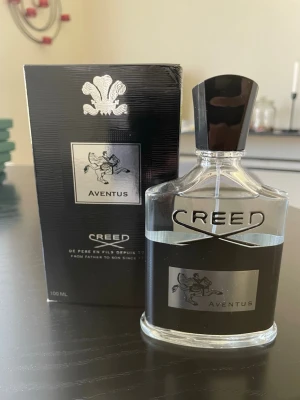 Creed Aventus Eau de Parfum 100ml - Creed Aventus är en exklusiv parfym i en stilren, genomskinlig glasflaska med svart och silverdetaljer. Flaskan rymmer 100 ml och har en svart kork. Doften är ikonisk och passar dig som vill sticka ut med en lyxig och modern parfym.