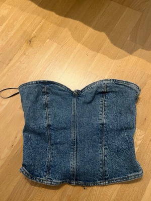 Denim korsett-topp med dragkedja - Trendig axelbandslös korsett-topp i blå denim med markerade sömmar och dragkedja bak. Jättesnygg!!!! Men tyvärr lite för stor för mig. 🫶🏼 Visar tecken på användning men är i ett gott skick i övrigt. Skulle säga att den passar både er som har strl S och M 