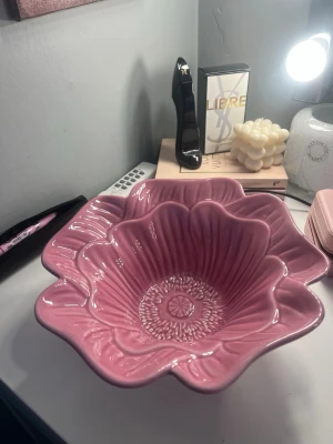 Rosa blomformad skål från Åhléns - Säljer en dekorativ skål i keramik från Åhléns, formad som en blomma och i en härlig rosa färg. Skålen har vågig kant och detaljerat mönster på insidan som liknar blomblad. Perfekt som inredningsdetalj eller serveringsskål.