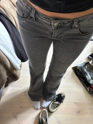 Grå bootcut jeans med låg midja - Säljer ett par grå bootcut jeans med låg midja och klassisk femficksdesign. Jeansen har en snygg tvättad look och är tillverkade i ett stretchigt denim-material som sitter bekvämt. Perfekta för dig som gillar en avslappnad och trendig stil.