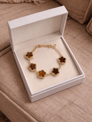 armband med bruna blommor - Snyggt armband i guldton med fem fyrklöverformade länkar i brun sten, inramade av små gnistrande detaljer. Länkarna är sammankopplade med en tunn kedja och armbandet har justerbar längd. Perfekt accessoar för dig som gillar unika smycken med elegant touch.