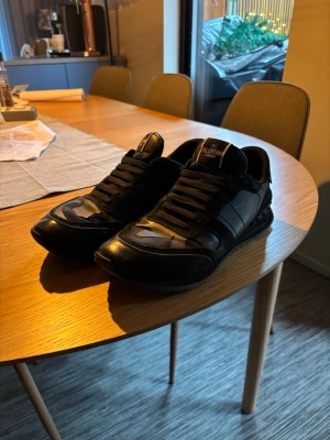 Valentino rockrunners  - Snygga svarta sneakers från Valentino med mattsvarta detaljer och coola nitar på hälen. Skorna har en låg profil, svarta skosnören och är tillverkade i en mix av läder och textil. Perfekta för dig som gillar stilrena och exklusiva sneakers.
