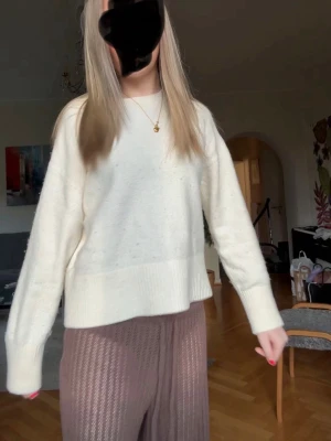 Vit stickad tröja med rund hals - Mysig vit stickad tröja med rund hals och långa ärmar. Tröjan har en avslappnad passform och ribbade muddar vid ärmslut och nederkant. Perfekt för lager på lager och enkel att matcha med olika stilar.