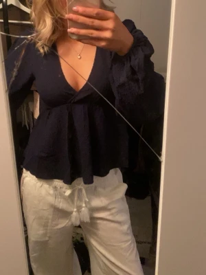 Mörkblå v-ringad blus med volangärm - Snygg mörkblå blus med djup v-ringning och volangdetaljer på ärmarna. Blusen har en lös passform och långa ärmar, perfekt för en trendig och avslappnad look.