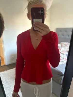 Röd omlott topp med knyt i midjan - Säljer en snygg röd omlott topp med v-ringning och långärmad design. Toppen har ett knytband i midjan som ger en cool och figurnära passform. Perfekt för dig som gillar att sticka ut med färg! Passar till många olika outfits.