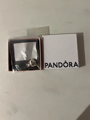 Pandora silverberlock katt - Säljer en söt berlock från Pandora i silver med katt formad design och en liten rosett i mitten. Perfekt att hänga på ditt armband för en personlig touch. Kommer i originalask. Säljer då det blev lite knas med våran beställning och vi fick en extra. Helt oanvänd och oöppnad!