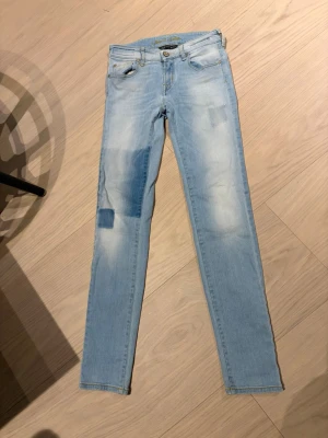 Ljusblå skinny jeans Jacob Cohen - Säljer ett par ljusblå skinny jeans från Jacob Cohen med patchade detaljer och slitningar på benen. Jeansen har klassisk femficksdesign, gylf med knapp och är tillverkade i stretchigt denimtyg för en bekväm passform.