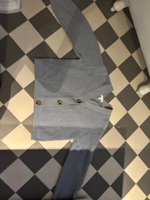 Ljusblå ribbad kofta med knappar - Snygg ljusblå ribbad kofta med stora bruna knappar framtill. Koftan har v-ringning, lång ärm och är gjord i ett mjukt stickat material. Perfekt att slänga över en t-shirt eller linne för en chill look. Från hm i storlek xs❤️