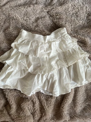 Vit volangkjol i bomull - Köpte på plick men aldrig använt! Supersöt vit kortkjol med flera lager volanger som ger en luftig och lekfull känsla. Kjolen är gjord i mjuk bomull och har en bekväm midja. Perfekt för dig som gillar en romantisk och trendig stil.