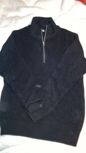 Svart stickad halvzip-tröja - Mörk stickad tröja från 157 med halv dragkedja och hög krage. Tröjan är ribbstickad och har långa ärmar samt breda muddar vid ärmslut och nederkant. Perfekt för lager-på-lager och chill dagar.