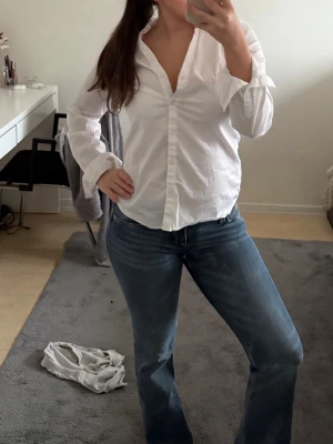 Vit klassisk skjorta från H&M - Säljer en vit klassisk skjorta från H&M med v-ringning och knappar framtill. Skjortan har lång ärm och är tillverkad i ett tunt, mjukt bomullsmaterial. Perfekt att styla till jeans eller kjol för en clean och enkel look.