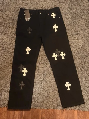 Chrome Hearts jeans  - Säljer ett par svarta Chrome Hearts-inspirerade jeans med vita och svarta korsdetaljer. Väldigt clean design och sticker ut bra. Helt nya med tags kvar. Skriv gärna för mer frågor!
