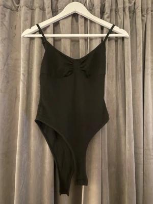 Svart body med smala axelband - Snygg svart body med smala axelband och lätt rynkad detalj vid bysten. Klassisk, enkel design som passar till mycket. Tillverkad i mjukt stretchigt material för skön passform.