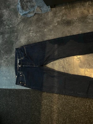 Mörkblå Levi's jeans 501 - Säljer ett par Levi's jeans med raka ben och fem fickor. Jeansen har snygga kontrastsömmar och den ikoniska levisdesignen på bakfickorna. Perfekta för dig som gillar tidlös stil och vill ha ett par jeans som funkar till allt.