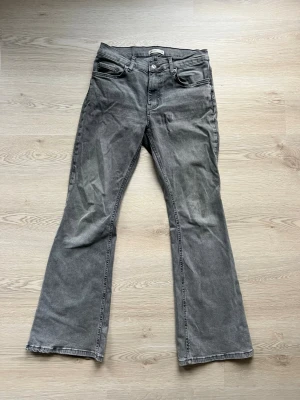Grå bootcut jeans från gina - Säljer ett par grå low bootcut jeans från gina. Jeansen har klassisk femficksdesign, knappstängning och bälteshällor. Materialet är mjukt denim och färgen är tvättad grå med lätt slitning. Perfekt för dig som gillar en avslappnad och trendig look.