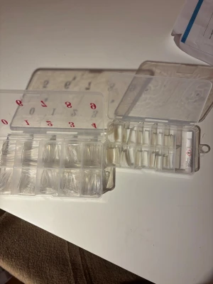 Transparenta och vita press-on naglar - Säljer två askar med press-on naglar i olika storlekar, både transparenta och vita. Perfekt för dig som vill fixa snygga naglar hemma! Naglarna är i plast och kommer i praktiska fack med siffror. Lim medföljer.