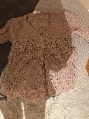 Beige virkad kofta från Odd Molly - Supersnygg beige virkad kofta från Odd Molly med vackra virkade detaljer och blommönster. Koftan har långa ärmar, v-ringning och knytning framtill. Perfekt för lager på lager och ger en bohemisk touch till din outfit.